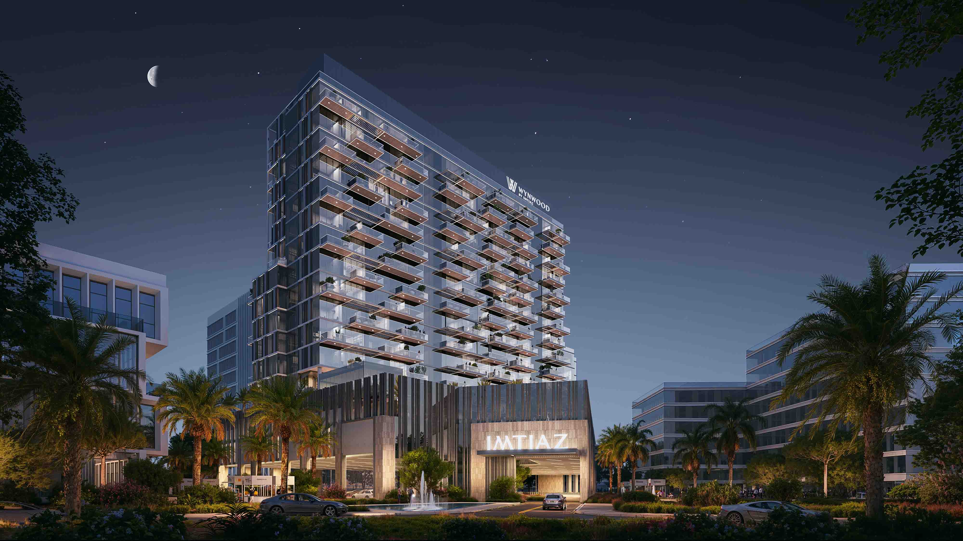 Wynwood By Imtiaz A modern building with glass balconies, surrounded by palm trees and lit up at night, featuring a stylish entrance.